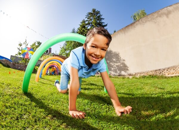 A child smiles while crawling through a foam noodle obstacle course in his backyard.