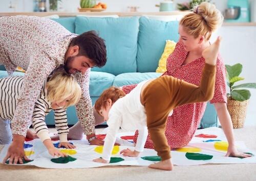 A family of two adults and two children play Twister at home. There are fun activities despite the stay at home orders.
