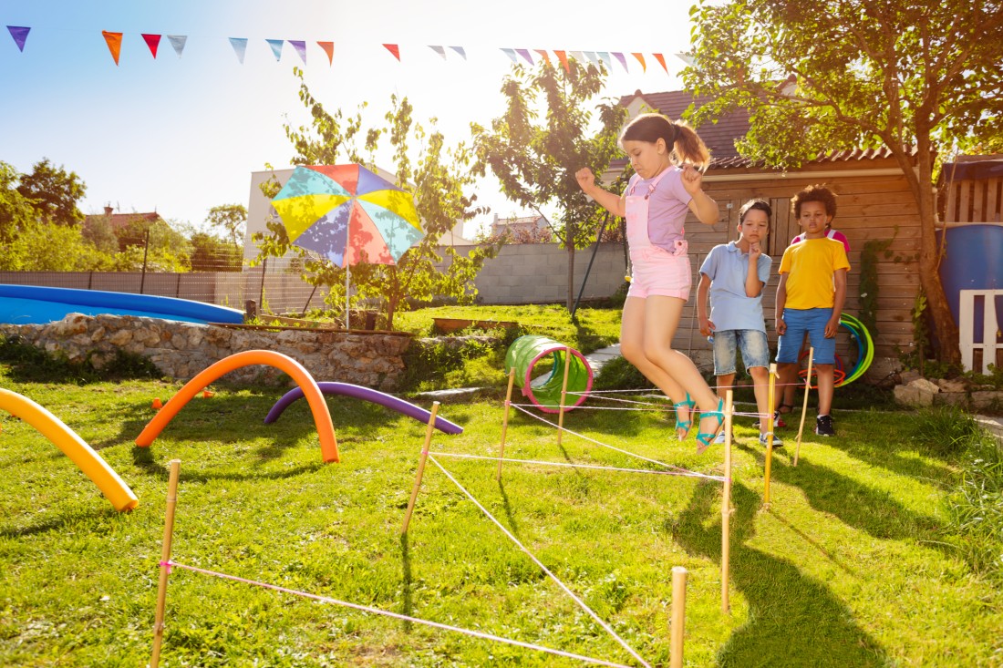 Three kids playing on an obstacle course with jumping games, tunnels, and other features.