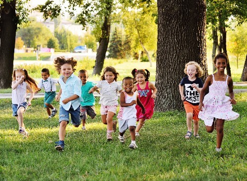 The importance of physical play for kids is felt in this picture of many children running in a park.