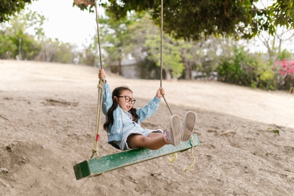 A kid plays on a swing set in a natural area.