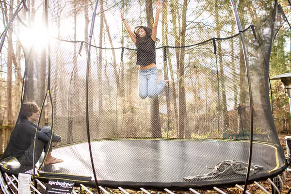 Kids jump for joy on a trampoline in their backyard. They are enjoying the last few nice days before the weather turns cold.