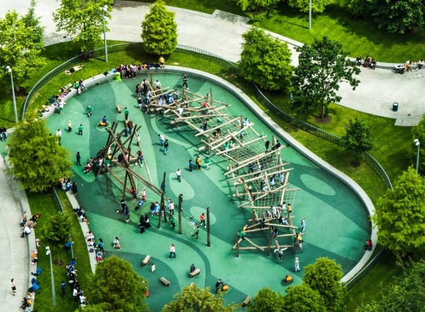 An aerial view of a kids' playground at a school shows teachers facilitating children having fun and working together.