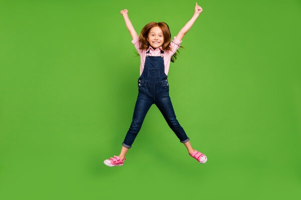 A young girl jumps for joy in front of a green background. 