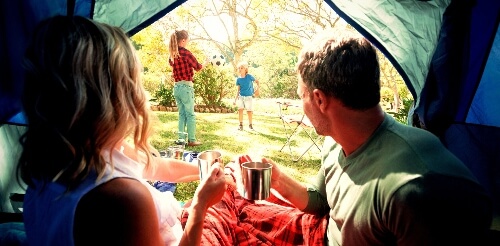 Two parents watch their kids play from inside a tent without stopping the kids' game.