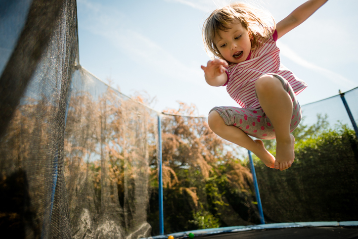 A child with autism and a big smile jumps on a trampoline in her backyard.