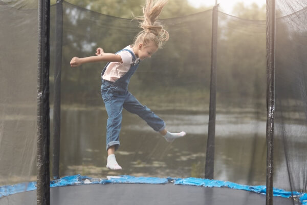 A young girl jumps on a trampoline protected by the safety net around the sides.